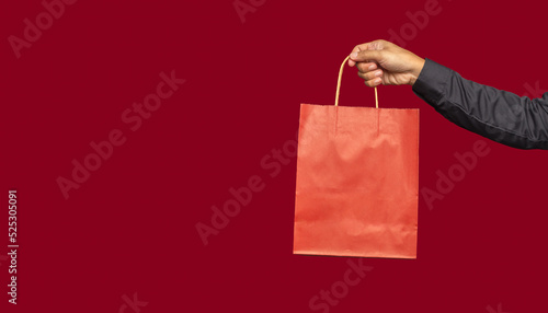 Hand holding a red paper bag with a handle while standing on a red background