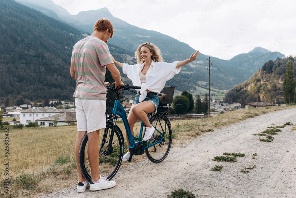 Fototapeta premium Two friends are cycling along the road. Sport and active life sunset time concept. Couple learning to ride a bike, having fun together, traveling in the mountains in the city