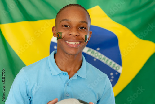 Portrait of happy african american male teenager with flag of brazil and football