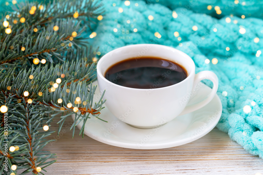 A cup of coffee, a plaid, and a Christmas tree branch in blurry lights A cup of coffee, a plaid, and a Christmas tree branch in blurry lights
