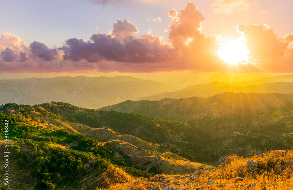 Obraz premium Mountain valley during sunset or sunrise. Rocks and slopes covered with green trees with amazing cloudy sunny sky on background.