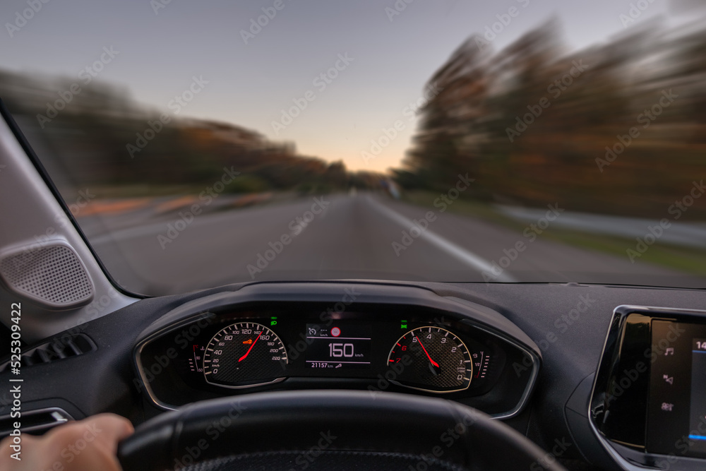 Driver view to the speedometer at 150 kmh or 150 mph and the road blurred in motion, night fall view from inside a car of driver POV of the road landscape.