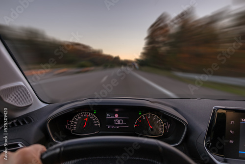 Driver view to the speedometer at 130 kmh or 130 mph and the road blurred in motion, night fall view from inside a car of driver POV of the road landscape.