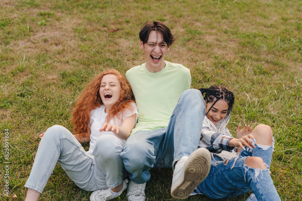 Three happy teenagers fell down on the grass while making a video to post on the internet. Funny moments. Influential bloggers on the internet Three happy teenagers fell down on the grass while making a video to post on the internet. Funny moments. Influential bloggers on the internet