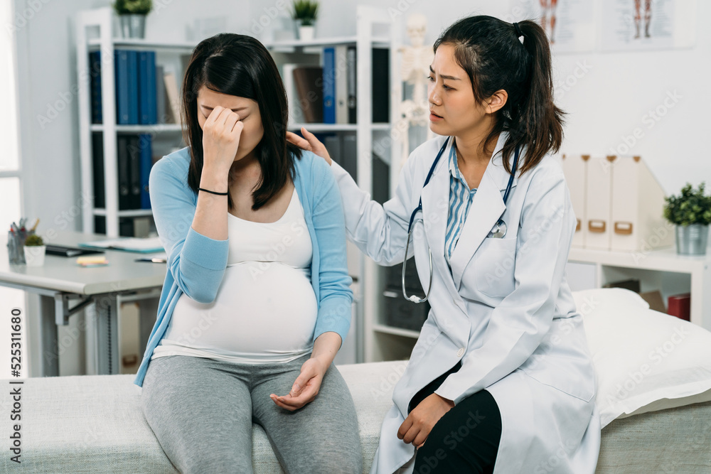 Obraz premium helpful asian female psychologist doctor is comforting and patting on the back of the sad expectant mom who’s covering her face on the treatment bed in hospital