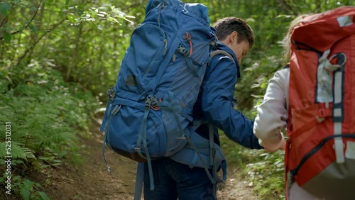 Wallpaper Mural Young man helps girlfriend to climb holding hand on footpath among trees. Male hiker shows pure love to young woman walking together in deep green forest Torontodigital.ca