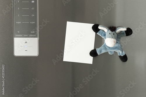 Blank sheet of paper on the refrigerator door with a funny refrigerator magnet that looks like a stuffed animal donkey 