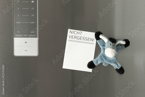 Notiz an der Kühlschranktür als Erinnerung mit einem lustigen Kühlschrankmagneten befestigt, der wie ein Stofftieresel ausssieht