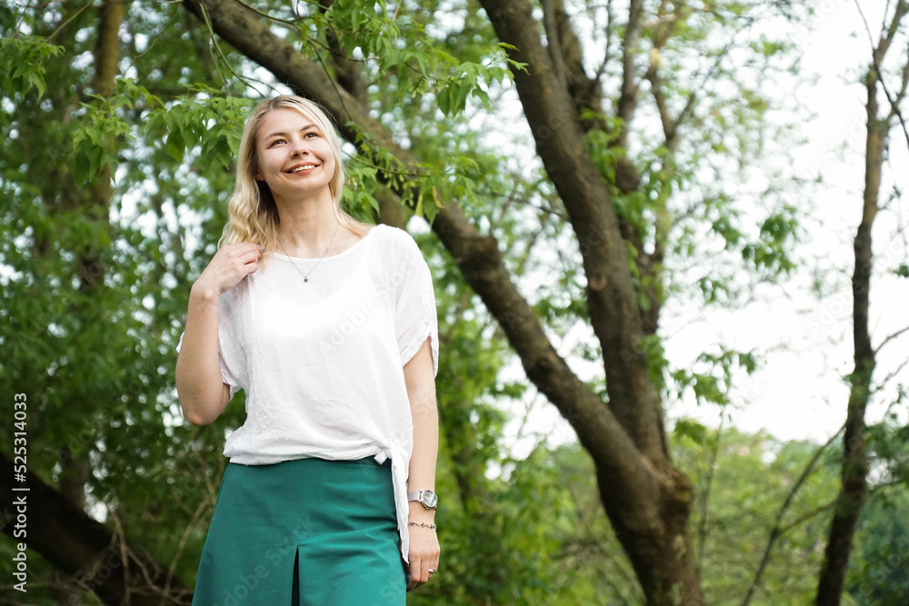 Beautiful young blonde in the forest. The girl enjoys nature on a summer sunny day against the background of green trees Beautiful young blonde in the forest. The girl enjoys nature on a summer sunny day against the background of green trees