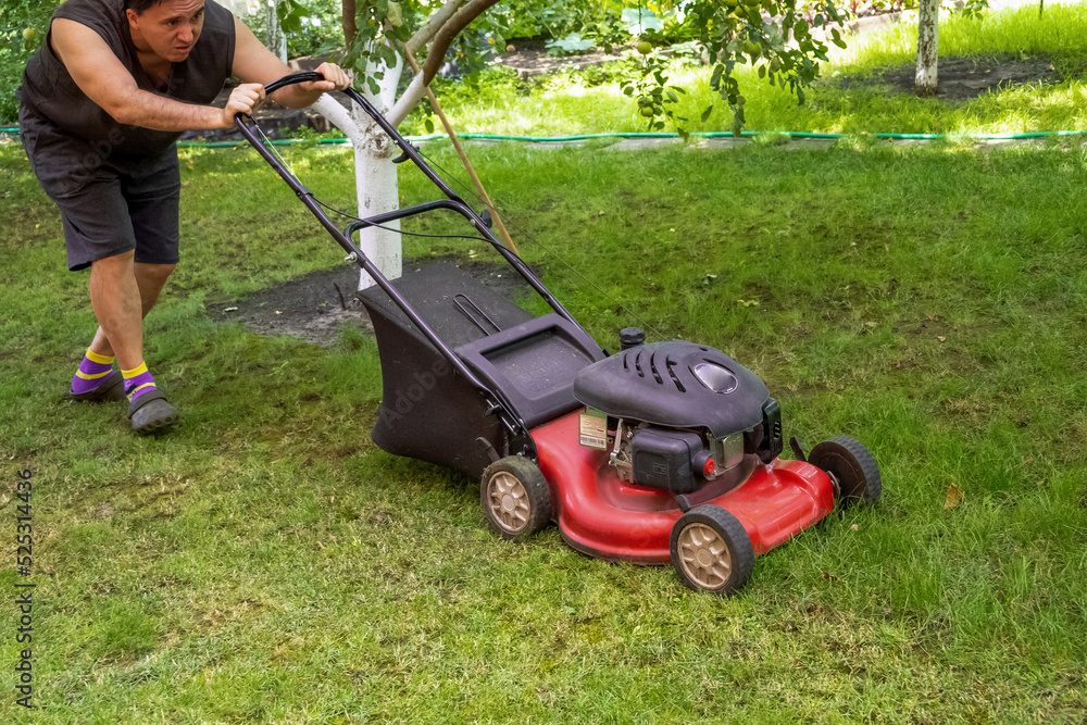 middle aged handsome man wearing home clothes is cutting the lawn, process to cut the grass at the yard with special machine lawn mover, green garden middle aged handsome man wearing home clothes is cutting the lawn, process to cut the grass at the yard with special machine lawn mover, green garden
