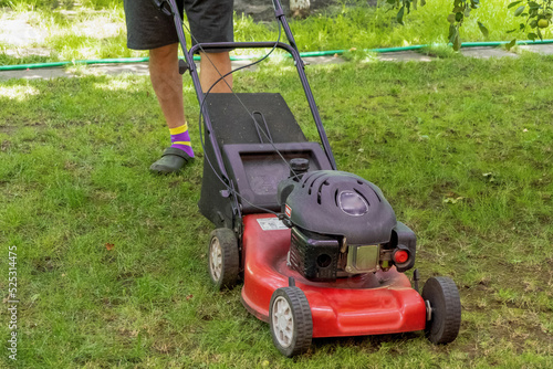 middle aged handsome man wearing home clothes is cutting the lawn, process to cut the grass at the yard with special machine lawn mover, green garden