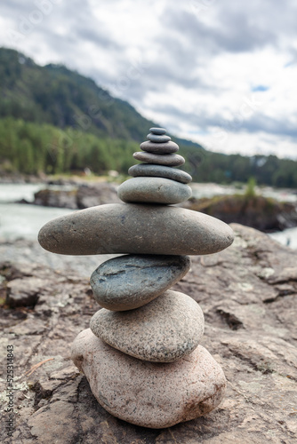 A pyramid of bare stones stacked on top of each other. Stones stacked in the shape of a pyramid on the riverbank against the background of mountains as balance and balance in nature  Zen  Buddhism.