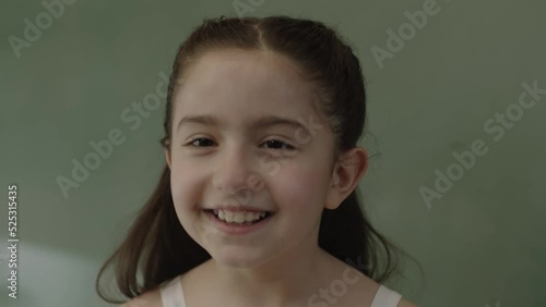 Little girl squinting her eyes having fun. Cute, funny and naughty little girl squinting in front of blackboard at school, smiling and looking at camera