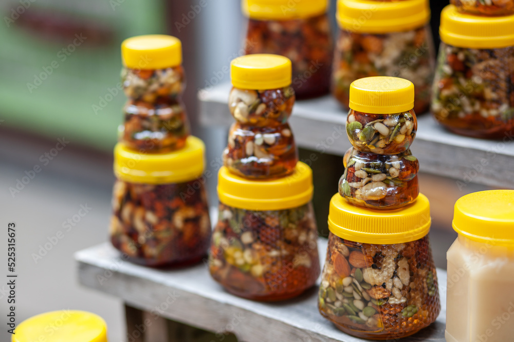 There are many jars of organic, natural honey on the counter for sale. Different honey, different colors in plastic cans are ready for sale at the honey fair. Nuts filled with honey. There are many jars of organic, natural honey on the counter for sale. Different honey, different colors in plastic cans are ready for sale at the honey fair. Nuts filled with honey.