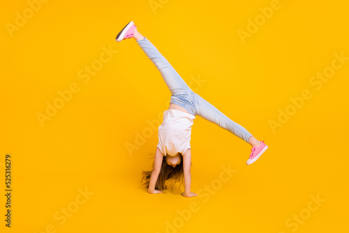 Full length photo of charming funny schoolgirl dressed white t-shirt walking hands upside down isolated yellow color background photo