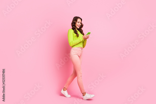 Full size photo of brunette lady go look telephone wear green shirt trousers shoes isolated on pink color background
