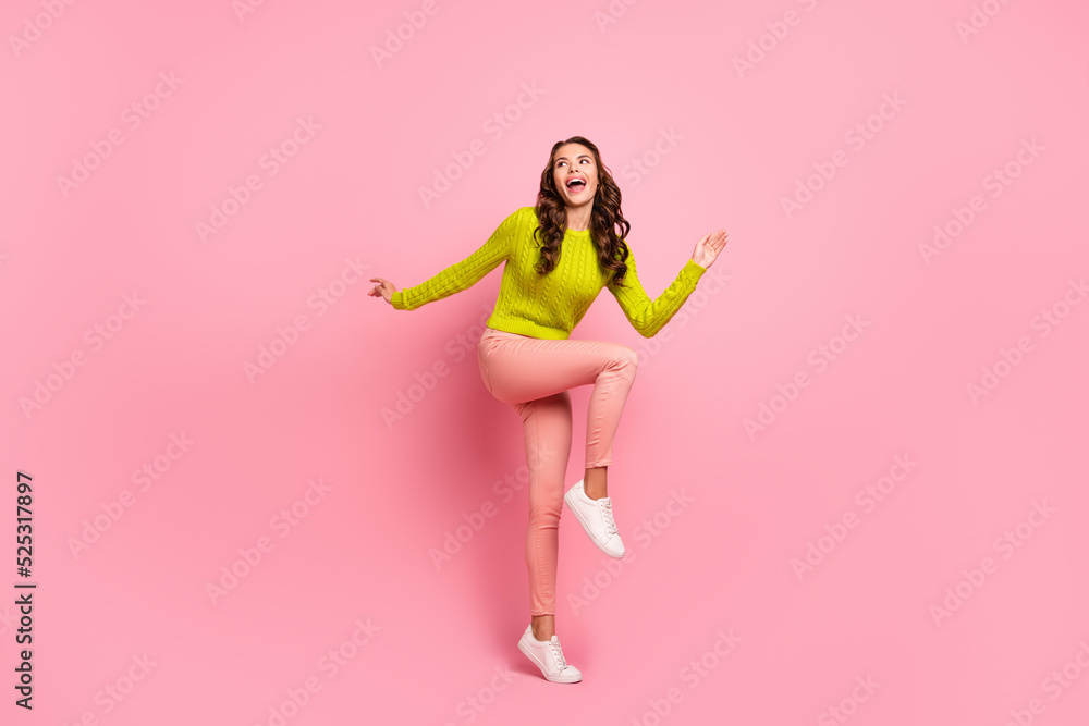 Full size photo of funky young lady jump look up wear green shirt pants boots isolated on pink color background Full size photo of funky young lady jump look up wear green shirt pants boots isolated on pink color background