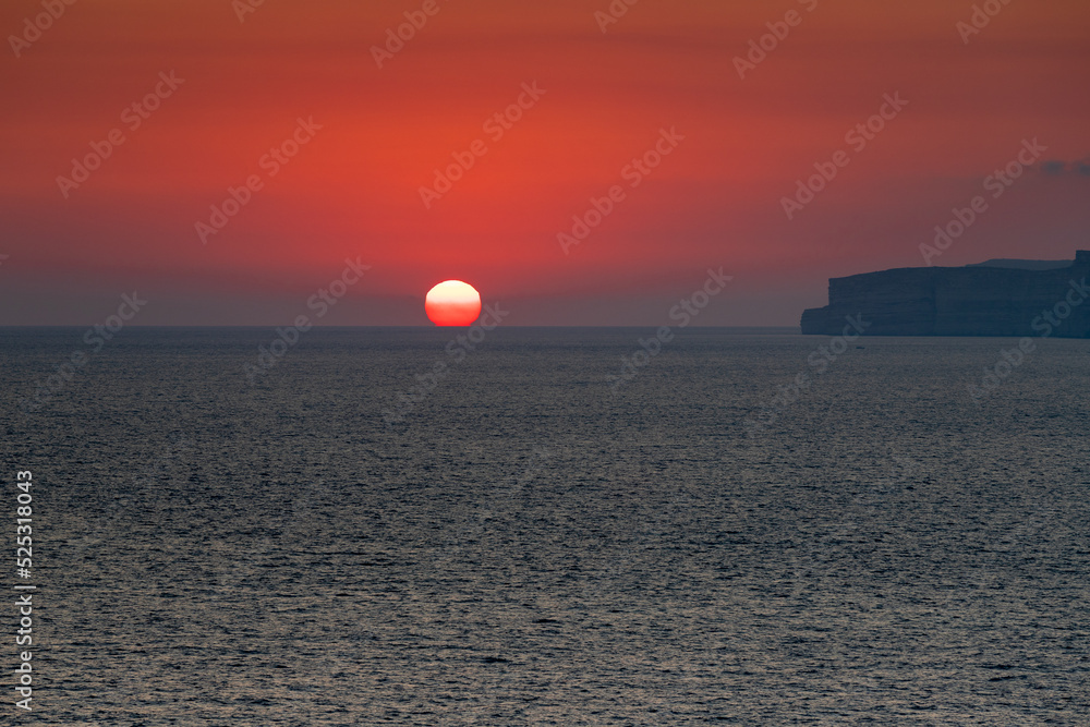 A colourful sunset over the cliffs of Paradis bay in Malta with a view on the Island of Gozo in the Mediterranean Sea. In summer the countries around the Mediterranean enjoy every evening these sunset