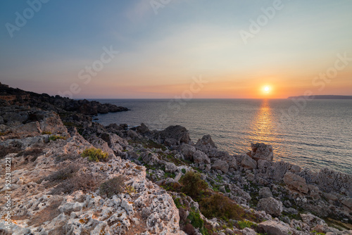 A colourful sunset over the cliffs of Paradis bay in Malta with a view on the Island of Gozo in the Mediterranean Sea. In summer the countries around the Mediterranean enjoy every evening these sunset © KimWillems