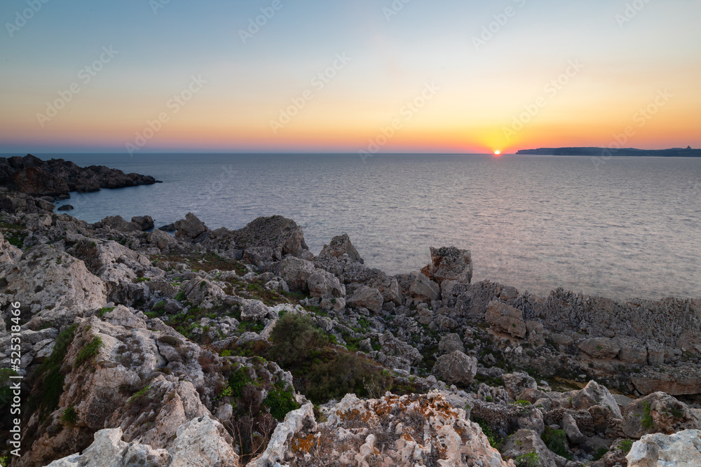 A colourful sunset over the cliffs of Paradis bay in Malta with a view on the Island of Gozo in the Mediterranean Sea. In summer the countries around the Mediterranean enjoy every evening these sunset