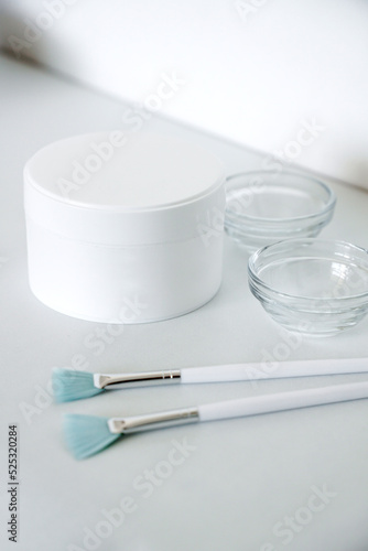 Skin care products at beauty salon mockup. Closeup shot of white plastic jar with face cream, glass bowl and peeling brushes on grey. Vertical photo photo