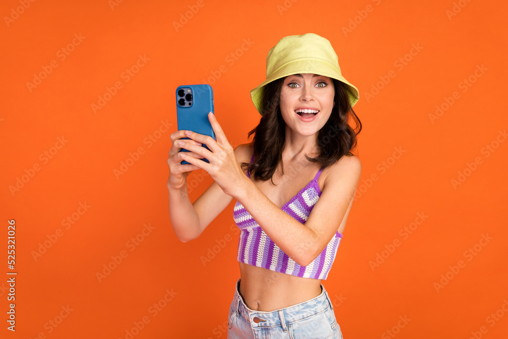 Photo of brunette impressed lady shoot picture wear hat top isolated on orange color background Photo of brunette impressed lady shoot picture wear hat top isolated on orange color background