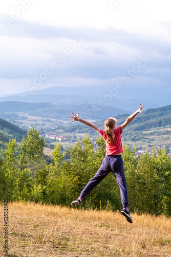 Beautiful Caucasian teenage girl jumping in a clearing against the backdrop of the Carpathian mountains.