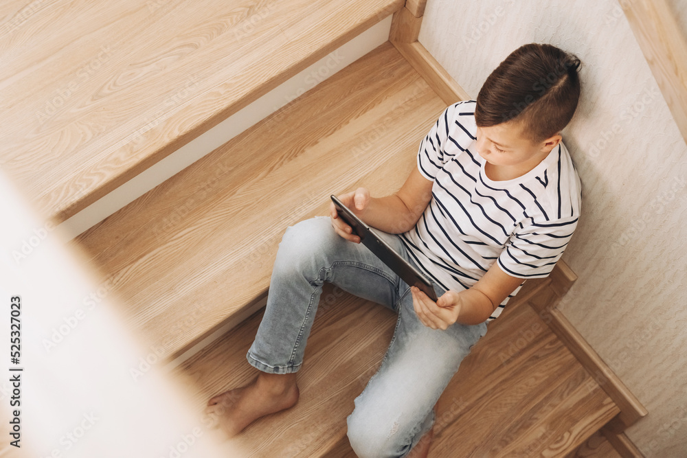 Teenage boy sitting on step of stairs using tablet playing video games on internet online at cozy home. Social media Teenage boy sitting on step of stairs using tablet playing video games on internet online at cozy home. Social media
