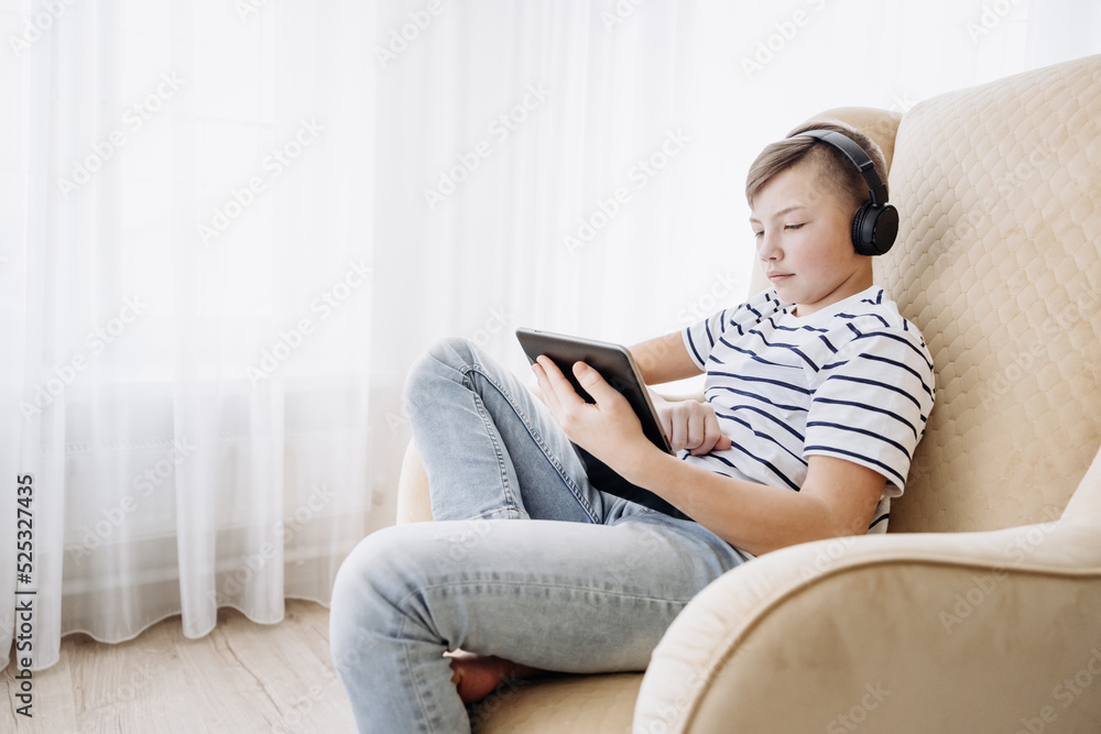 Teenage boy in wireless headphone using tablet having video chat on internet online at home. Child watching movie, playing video game. Social media concept. Online education. Distance learning Teenage boy in wireless headphone using tablet having video chat on internet online at home. Child watching movie, playing video game. Social media concept. Online education. Distance learning