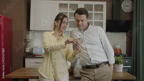 Happy couple using smartphone at dining table in kitchen,checking bank accounts,shopping online,checking social networks, ordering food from restaurant. They show the green screen phone to the camera. photo