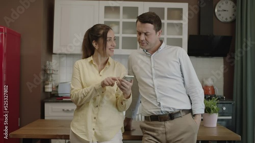 Happy couple using smartphone at dining table in kitchen,checking bank accounts,shopping online,checking social networks, ordering food from restaurant. They show the green screen phone to the camera. photo