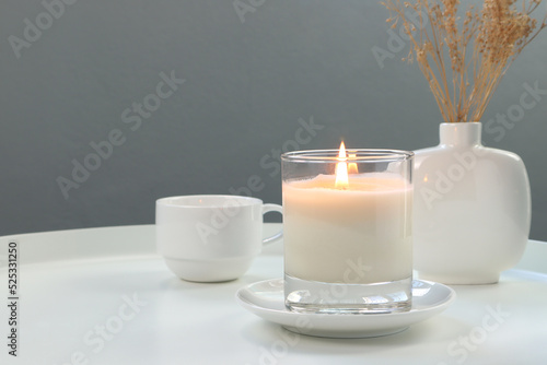 luxury lighting aromatic scented candle is on white metal table with ceramic vase and a coffee cup to creat relax ambient in the livingroom with background of nice grey cement wall on Valentine day