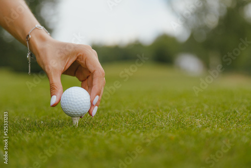Woman's hand with a manicure puts a golf ball on a tee on a golf course