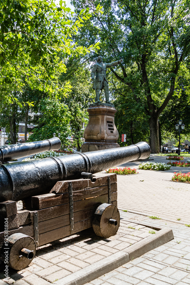 Old ship guns near monument to Peter I in Petrovsky Square. Majestic bronze statue of Russian emperor on pedestal of pink Pavlovsk granite. Voronezh, Russia - July 30, 2022