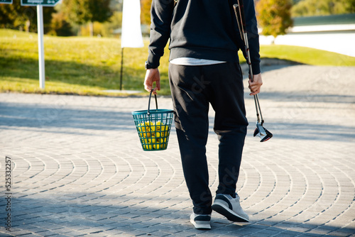 Golfer carries clubs and a bucket of balls