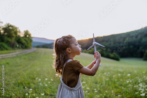 Little girl standing in nature with model of wind turbine. Concept of ecology future and renewable resources. photo