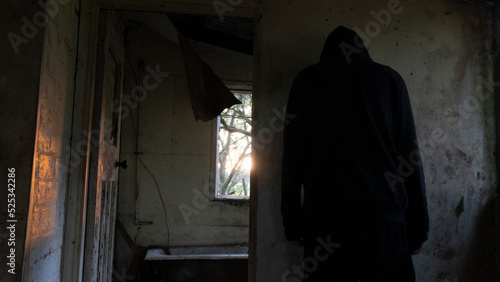 A spooky strange concept of a hooded man back to camera facing a wall. In a scary abandoned house.