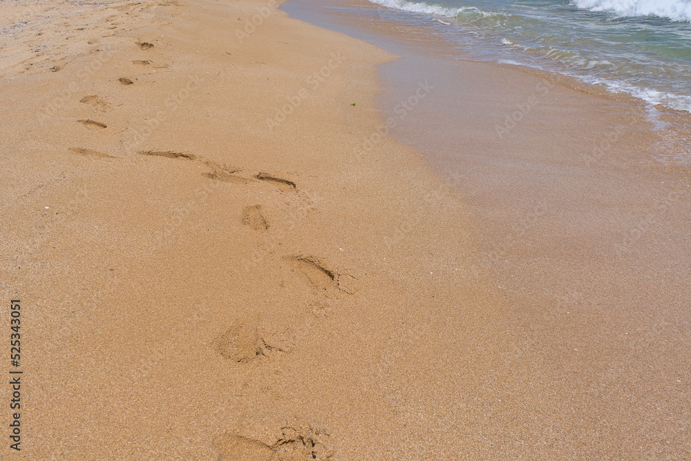 Clear emerald green sea with white foam and yellow sand on the beach with human footprints Clear emerald green sea with white foam and yellow sand on the beach with human footprints