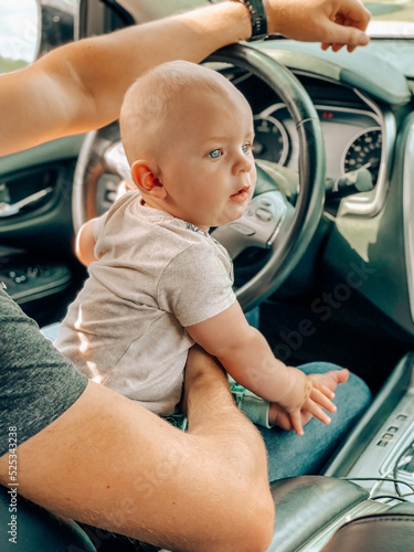 Cute baby boy 8 month old with his father driving car near the stearingwheal