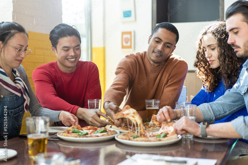 Smiling friends eating pizza at modern pizzeria restaurant - Friendship concept with multi ethnic people enjoying time together having fun at pizzeria with pizza and beer pints