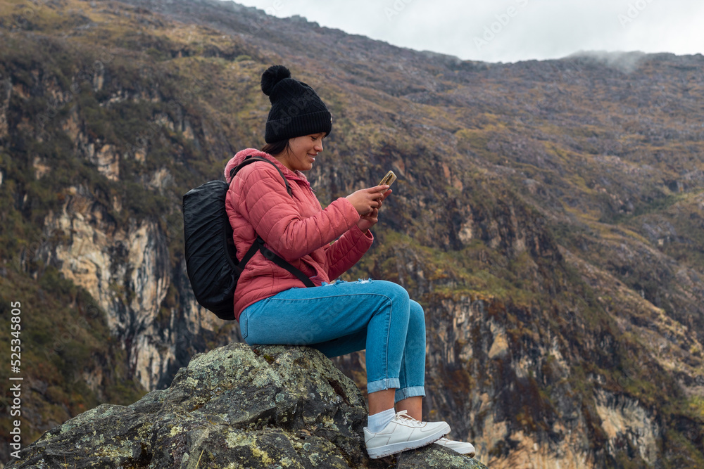Excursionista atractivo sentado y sosteniendo un teléfono junto a un lago tranquilo en las hermosas montañas