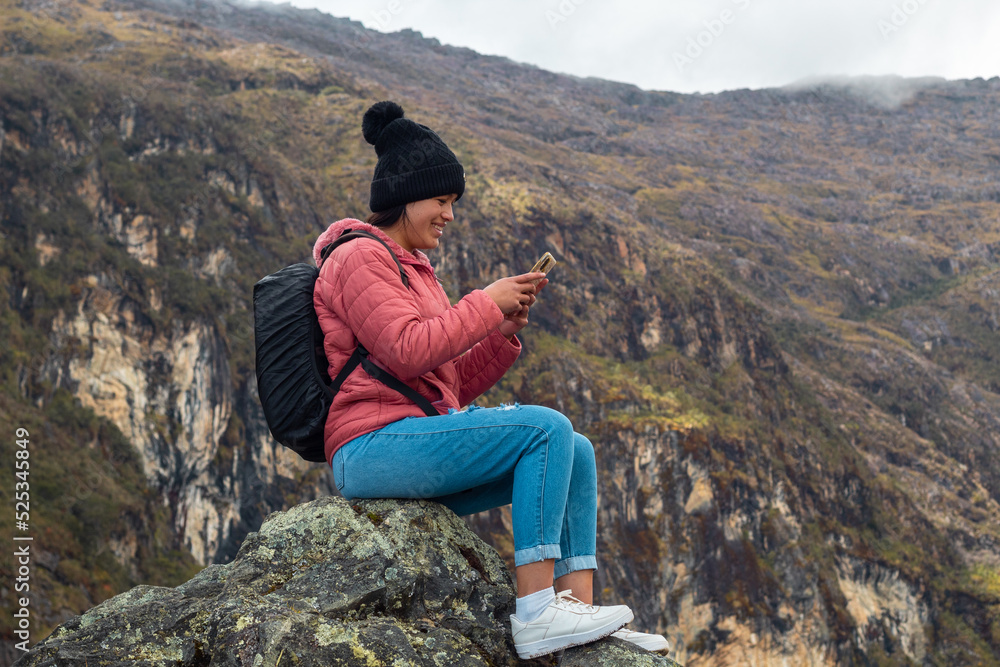 Excursionista atractivo sentado y sosteniendo un teléfono junto a un lago tranquilo en las hermosas montañas
