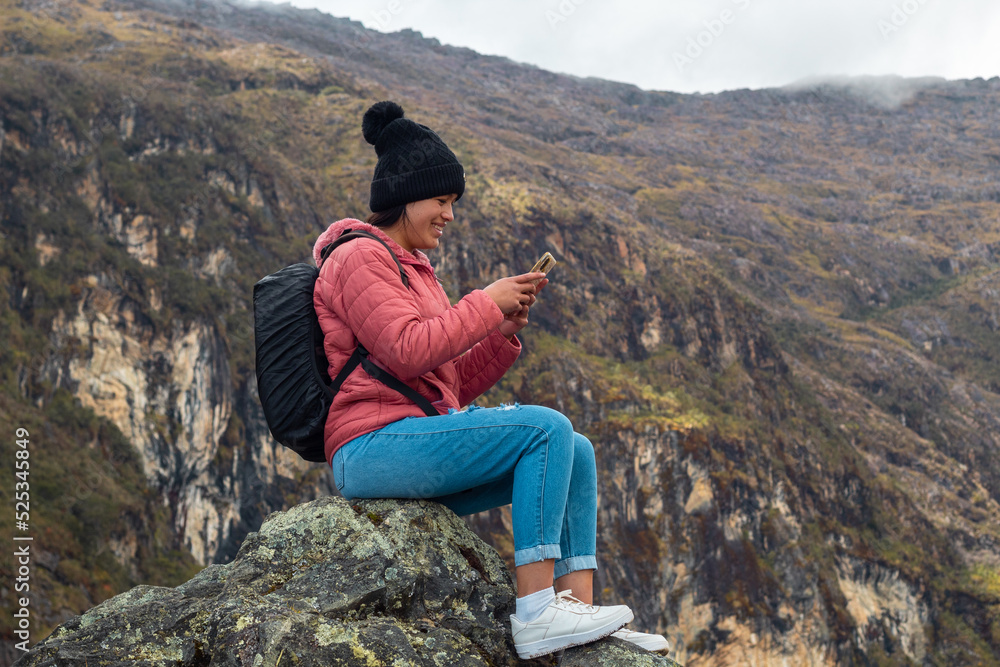 Naklejka premium Excursionista atractivo sentado y sosteniendo un teléfono junto a un lago tranquilo en las hermosas montañas