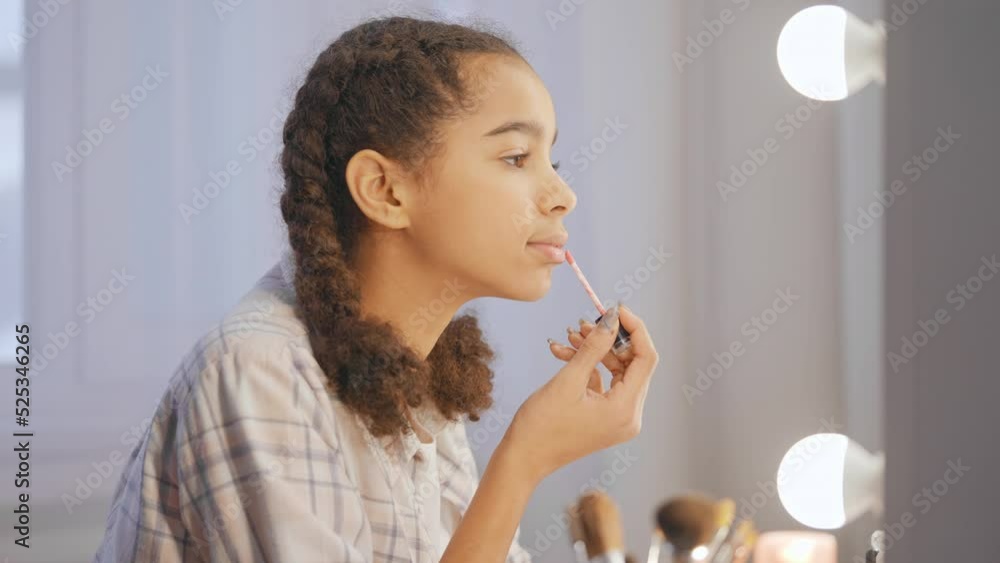 African American teenage girl applying lip gloss in front of mirror, adolescence African American teenage girl applying lip gloss in front of mirror, adolescence