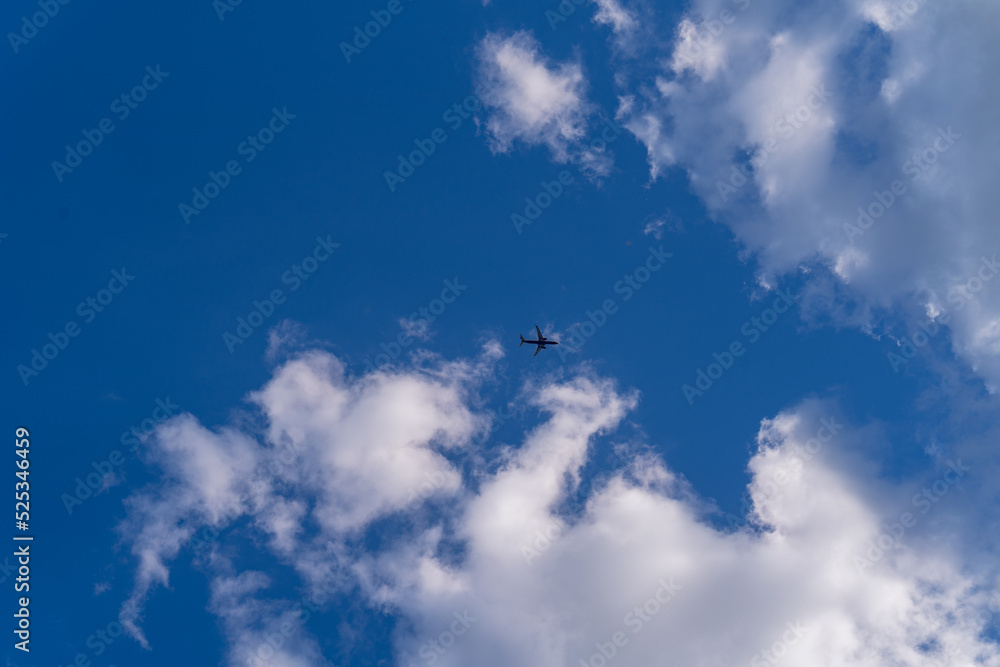 a plane flying against the background of a blue sky with beautiful white clouds, a photo from below, the plane is far away in the photo, the sun is shining from behind the clouds a plane flying against the background of a blue sky with beautiful white clouds, a photo from below, the plane is far away in the photo, the sun is shining from behind the clouds