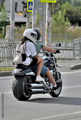 A man and a woman ride a motorcycle down the street on a summer day