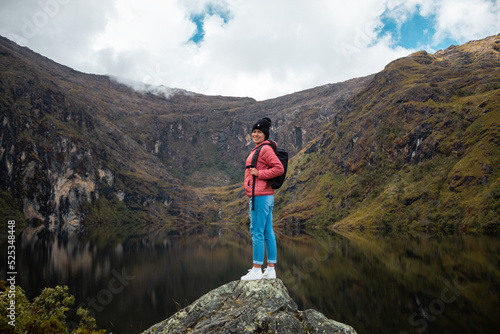 Una chica con una chaqueta rosa y mochila parada junto a un tranquilo lago en las hermosas montañas