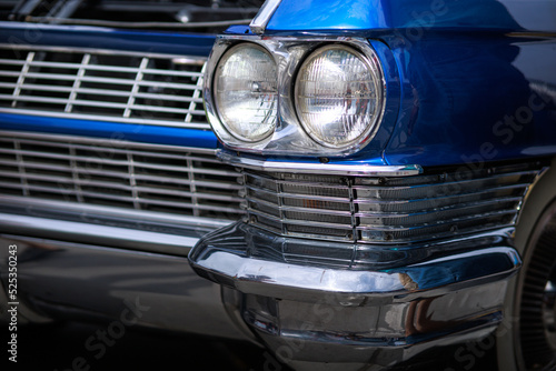 The front quarter panel, headlight housings, and chrome grill and bumper, and white wall tire of a vintage classic blue auto. photo