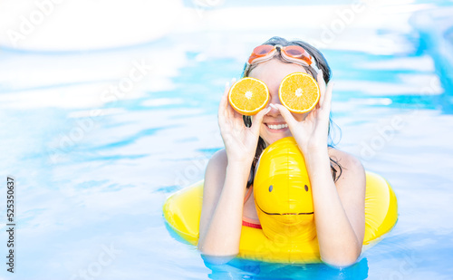 Happy teen girl in swimming pool with inflatable toy duck holds orange like eyeglasses. Empty space for text
