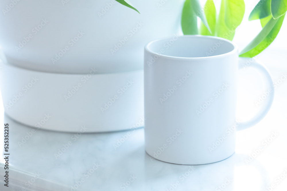 A white mug on the windowsill near the plant. White soft minimalist high key picture.